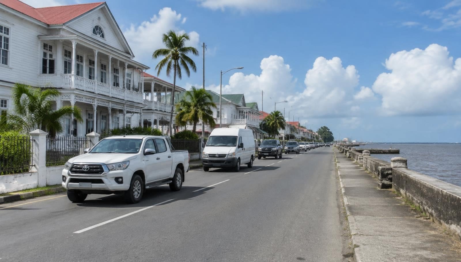 Pickups and a van on a seawall road lined with colonial buildings in Georgetown, Guyana